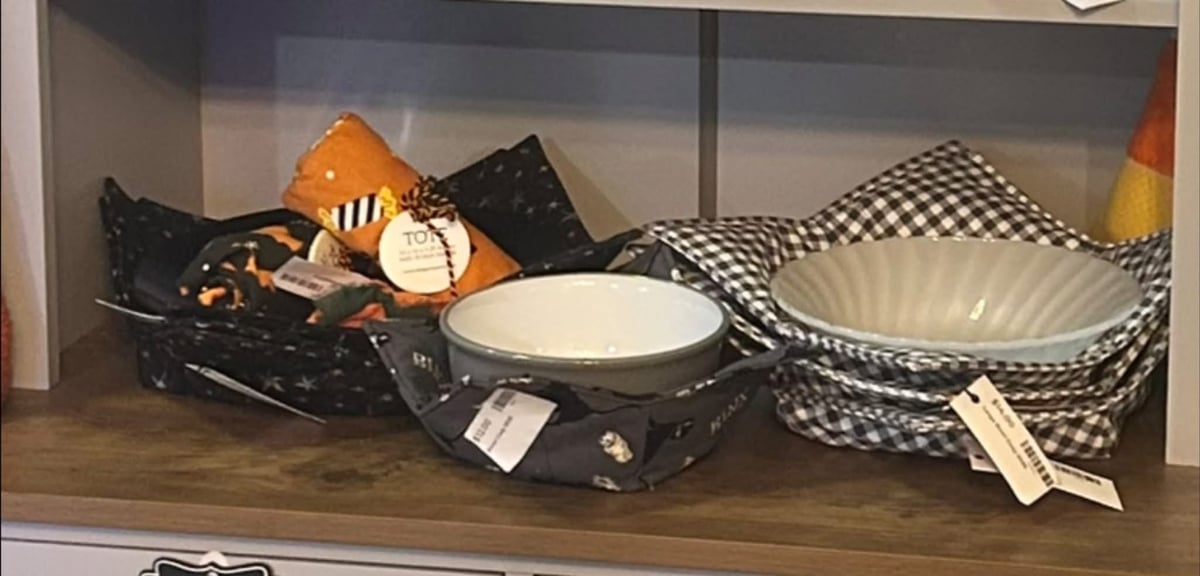 Display of Halloween-themed tableware and decorations including orange pumpkin, black checkered pattern items, white bowls, and festive skull design on wooden shelf