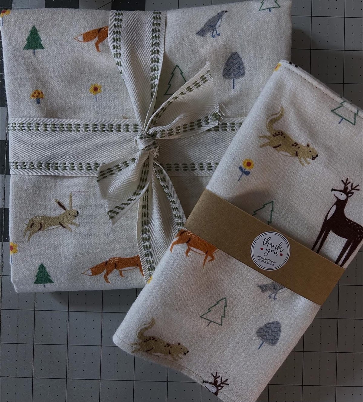 Set of woodland-patterned cloth napkins and tea towel featuring forest animals and trees, tied with striped ribbon